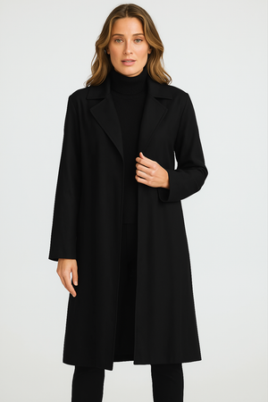 A model wearing a knee-length black trench coat with a lapel collar and side seam pockets, standing against a white backgroun